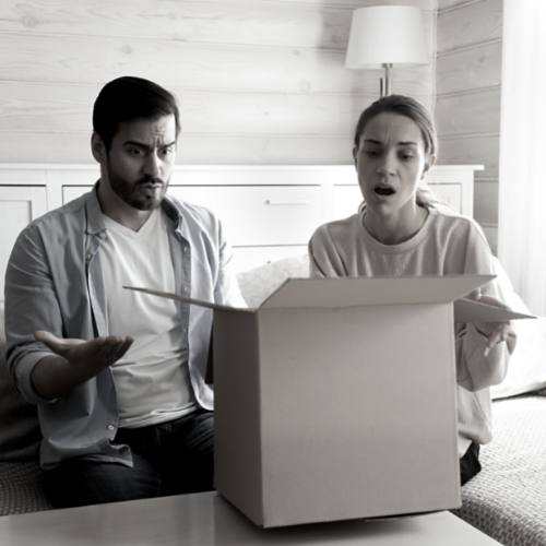 A man and and woman seated looking into a large brown box with looks of shock and displeasure unsure of what the return and refund policy is.