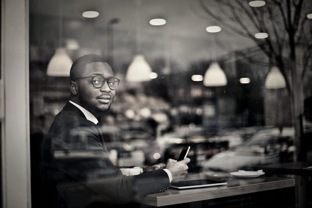 A man dressed in a business suit, mobile phone in hand as he is seated as at table looking out a large window with a curiously knowing look on his face. Contemplating the alternative after reading the Ethical Insights