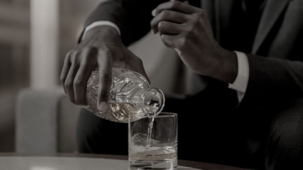 Male hand pouring alcohol from a crystal decanter as he gets comfortable for a Humming Session