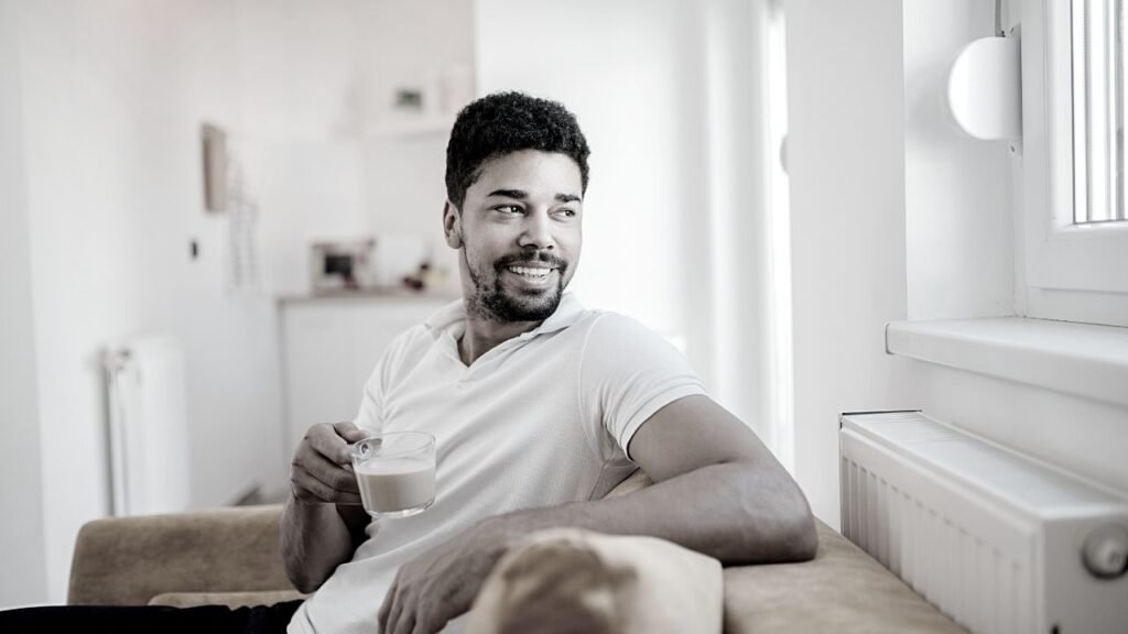 A man relaxing with a cup of hot beverage smiling as he looks out the window