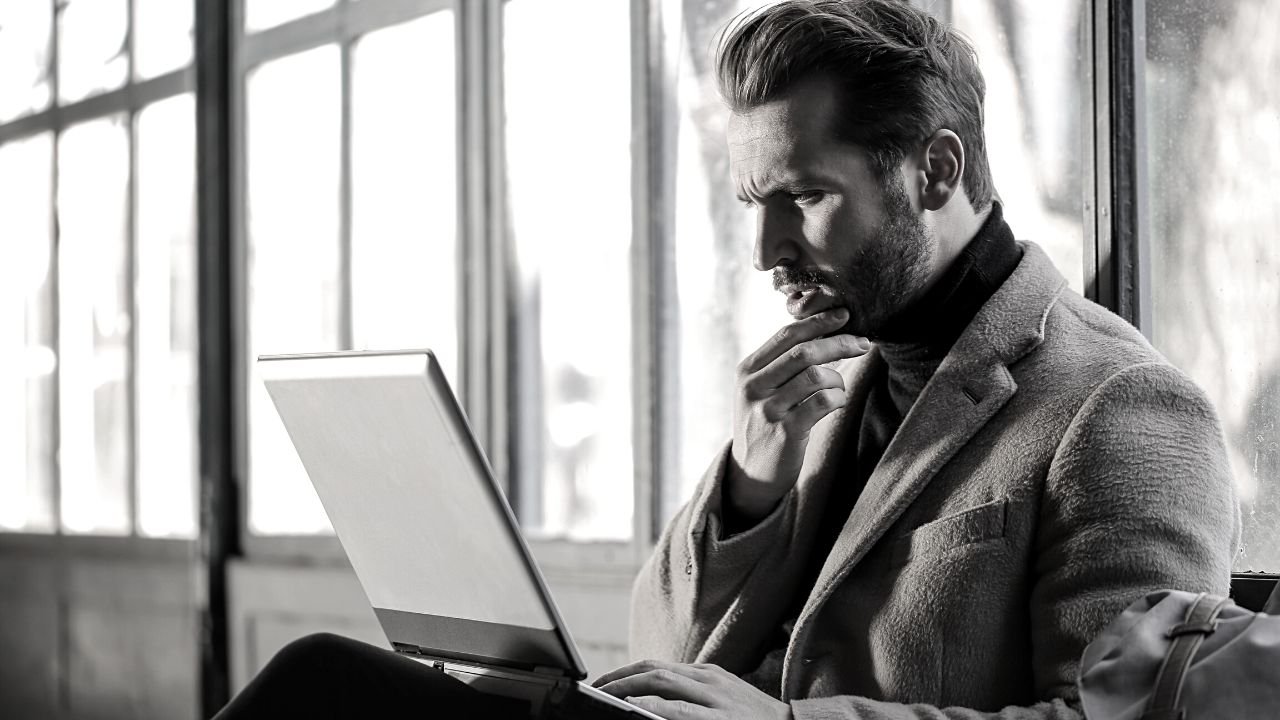 Man seated with perplexed express looking at laptop hold his chin. Introducing policies to an online business will bring clarity.