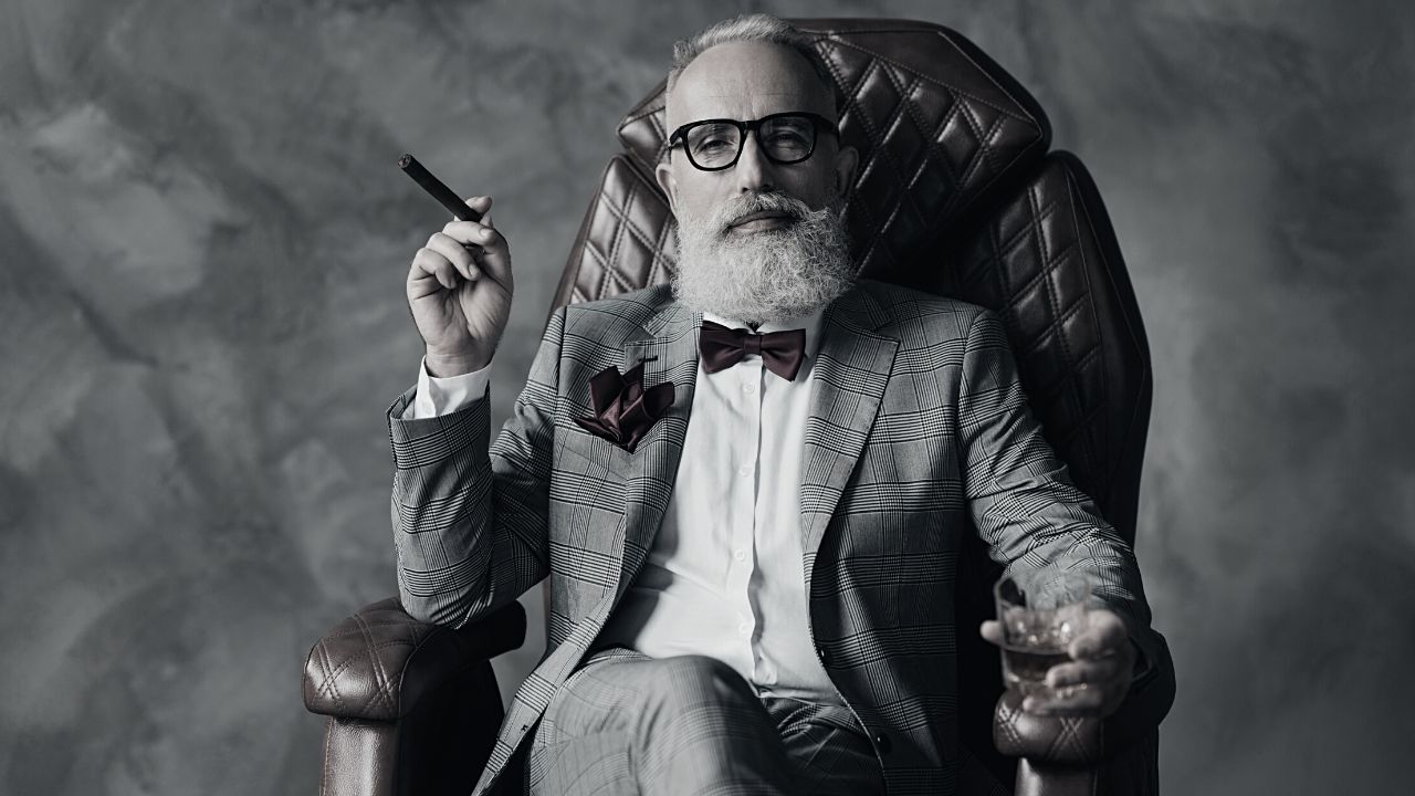 A mature man relaxed in an armchair smoking a cigar wearing a tweed suit bow tie and dark rimmed glasses. Once you understand you'll have the confidence to run business your way.